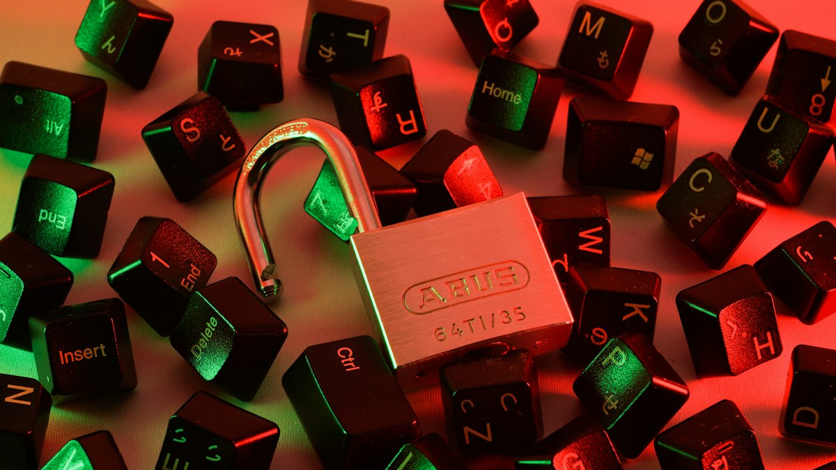 An open padlock lying among scattered computer keyboard keys under red and green light